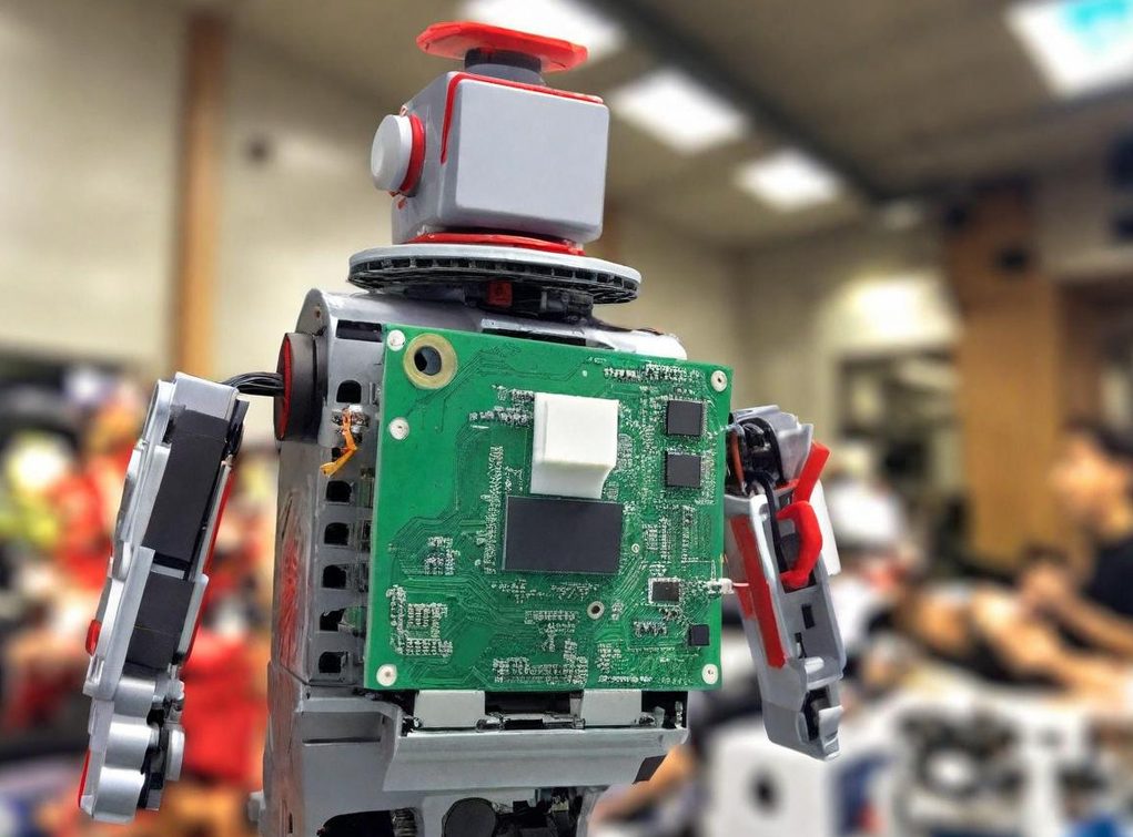 A small robot with a circuit board as its torso, set in a workshop environment.